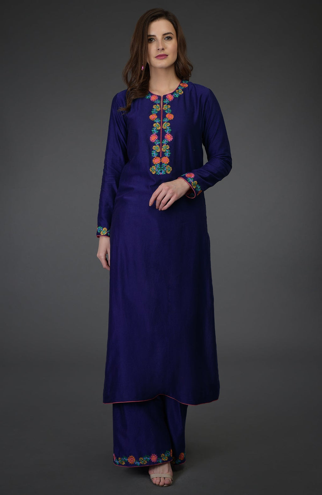 A woman models a blue palazzo suit with colorful floral embroidery.