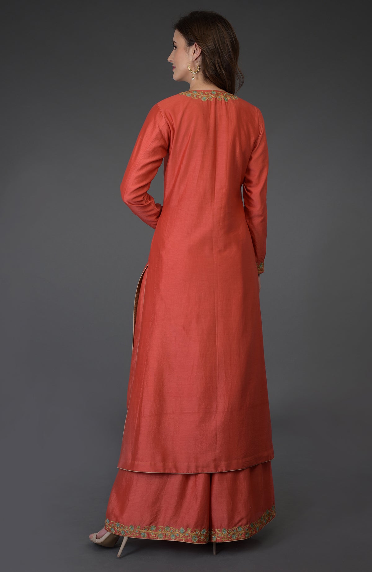 A woman models a coral resham-tilla embroidered farshi palazzo suit from the back.
