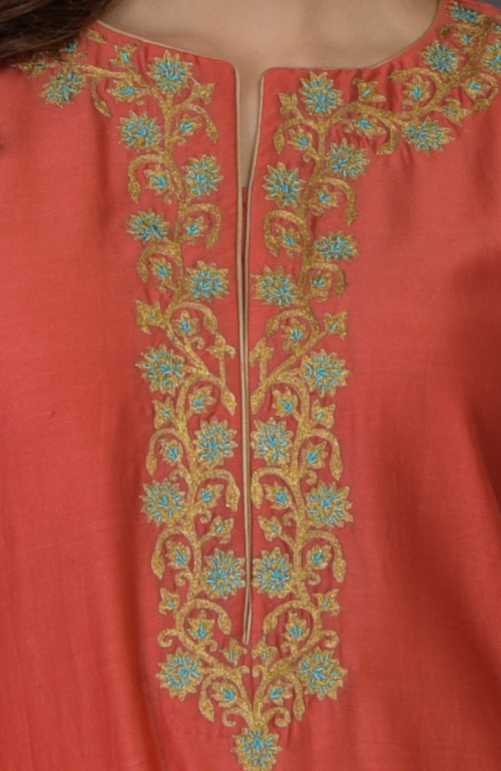 A close-up of a living coral suit with gold and blue floral embroidery.