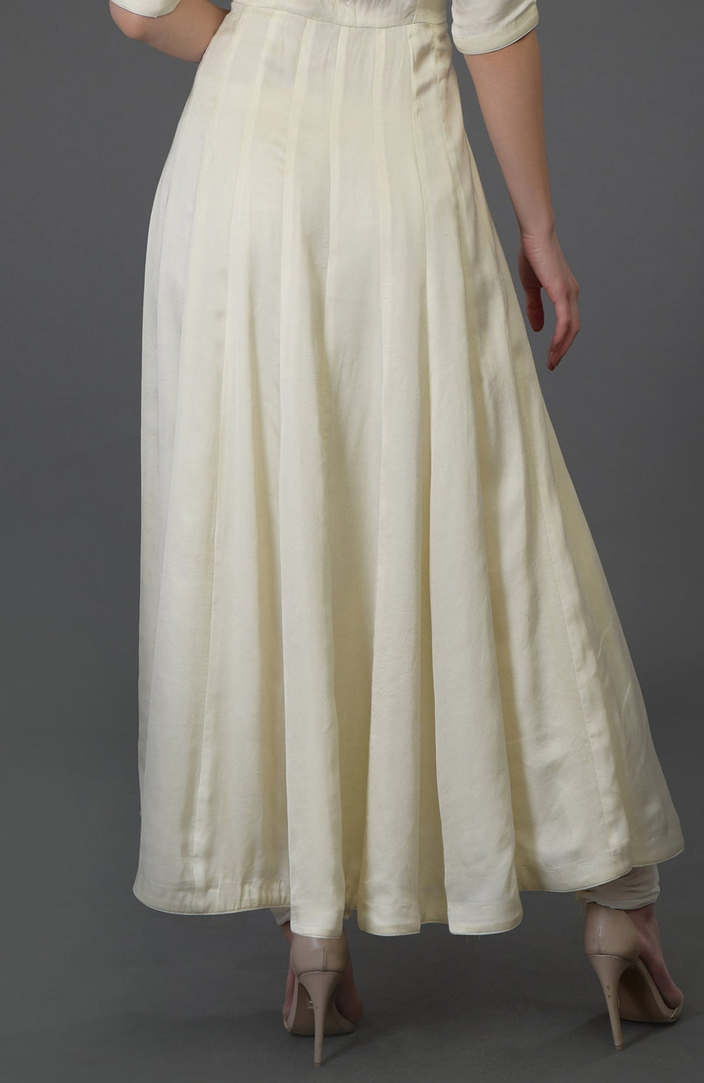 A woman from the back wearing an ivory anarkali suit and nude heels.