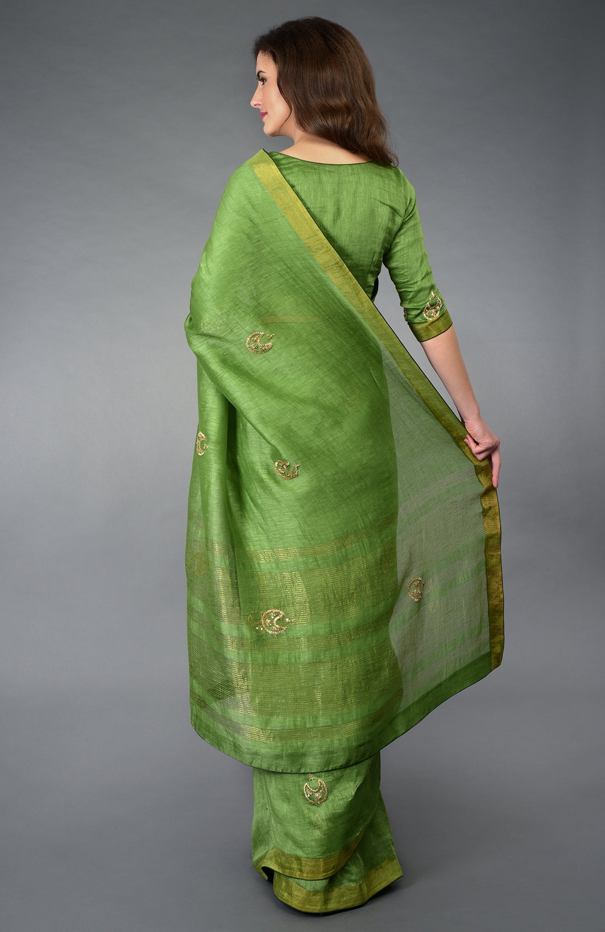 A woman models a pepper stem green linen saree with gold embroidery and borders.