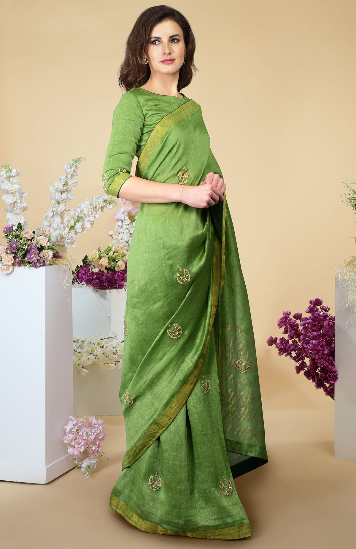 A woman models a pepper stem green linen saree with gold embroidery and zari borders.