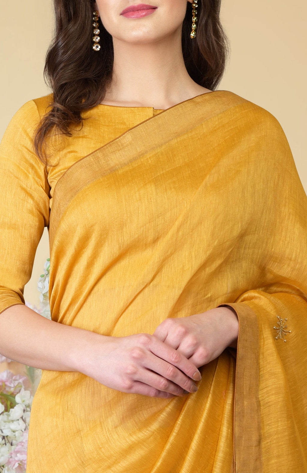 A woman in a citrus yellow linen saree with gold embroidery and brown borders.