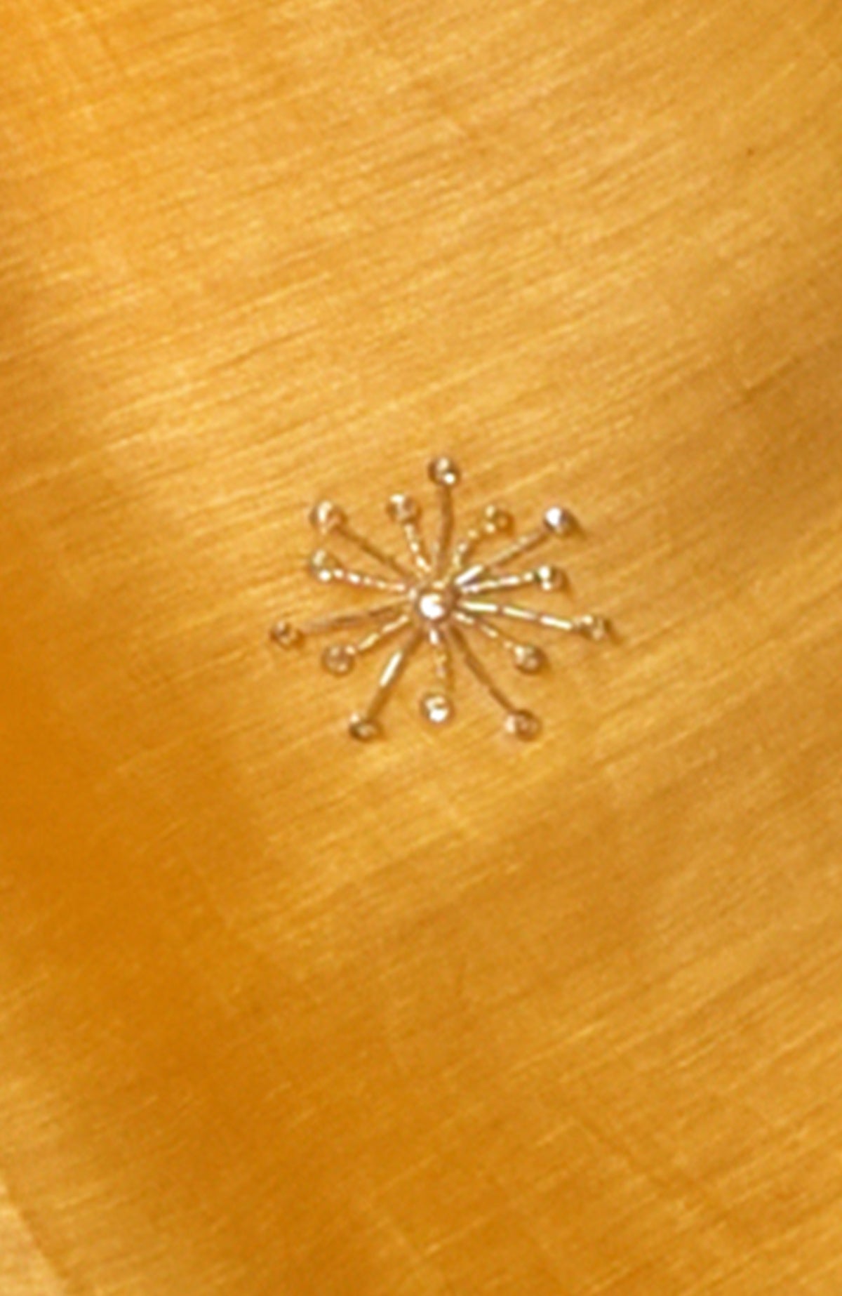 Close-up of a gold zardozi hand-embroidered motif on citrus linen fabric.