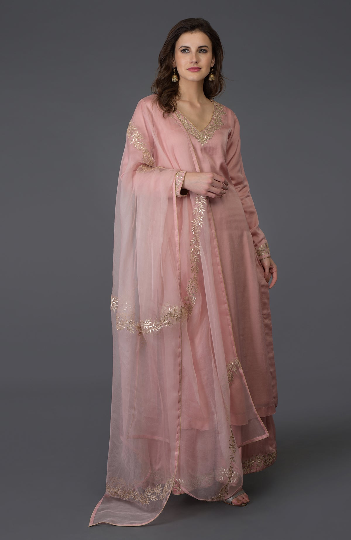 A woman models a pearl pink gota patti work farshi palazzo suit with a sheer dupatta.