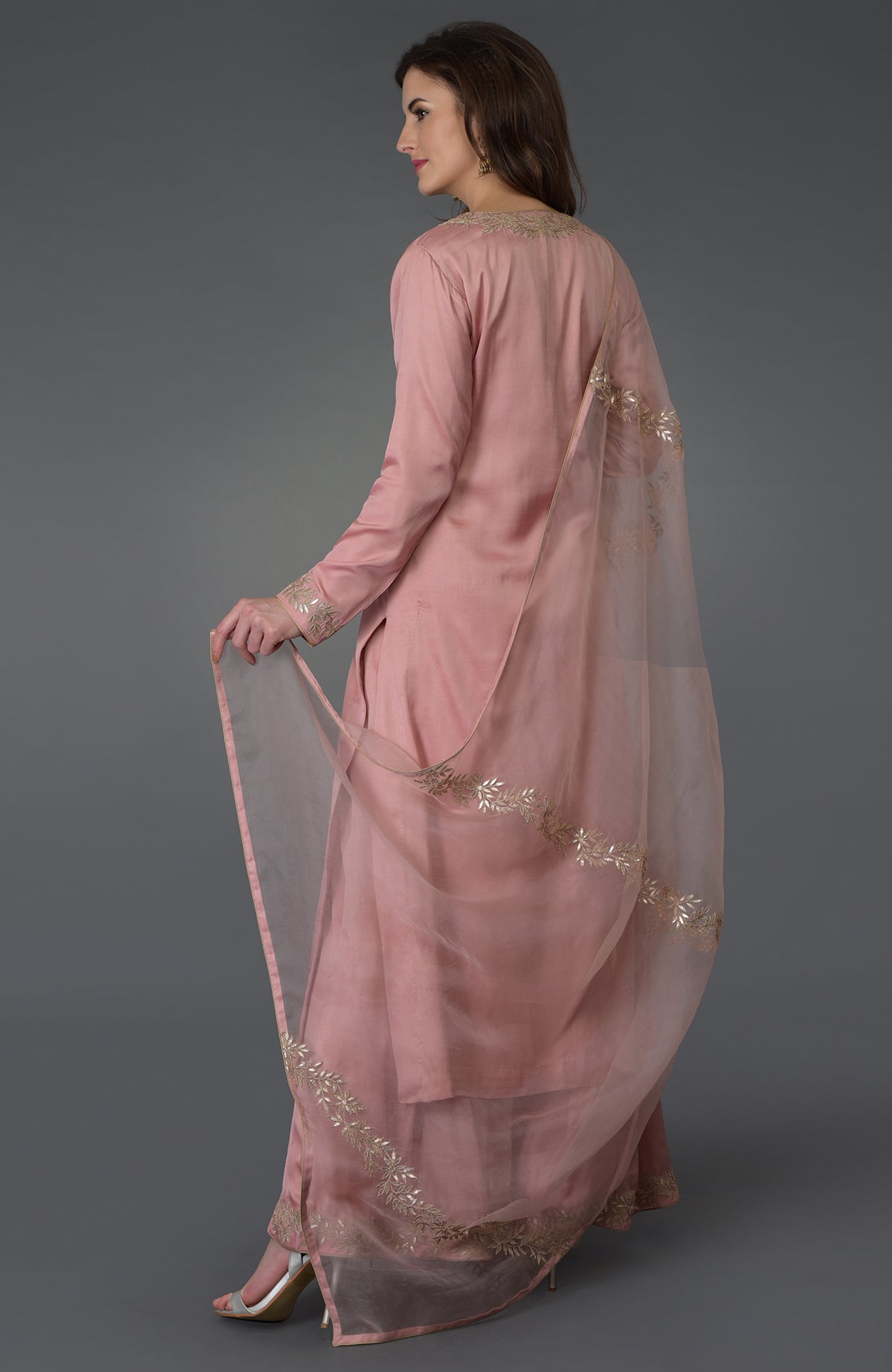 A woman in a pearl pink gota patti work farshi palazzo suit with an embroidered dupatta.