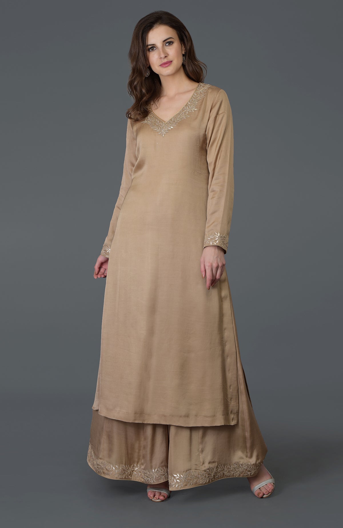 A woman models a beige gota patti work farshi palazzo suit with embroidery.