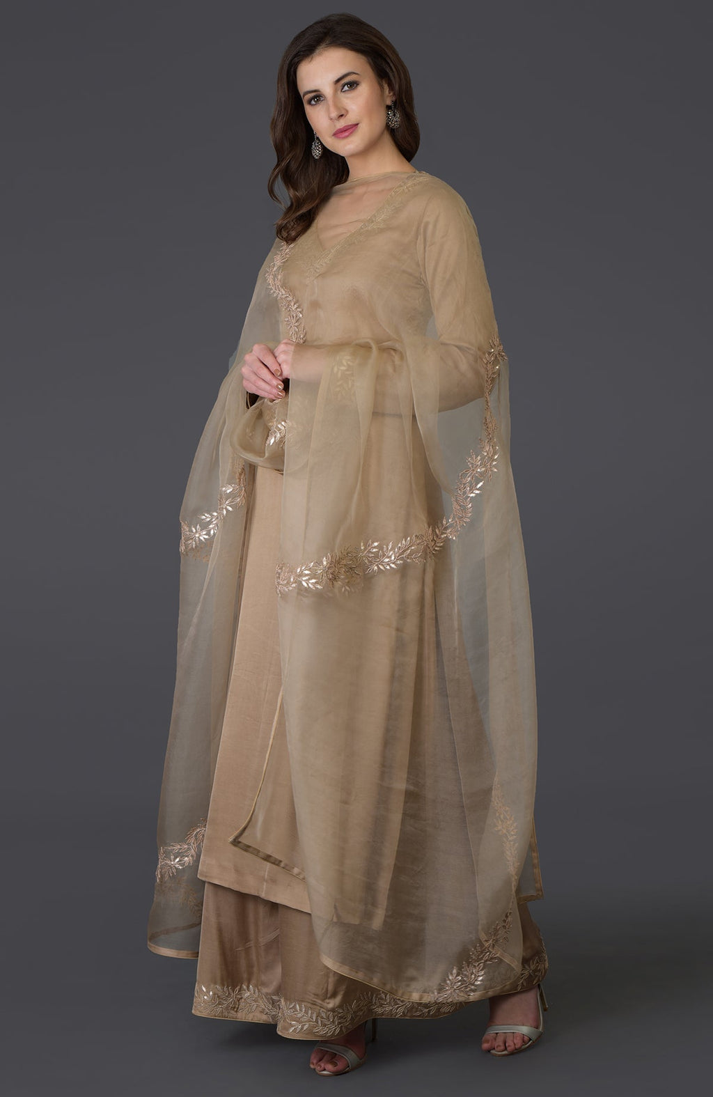 A woman models a beige Gota Patti work farshi palazzo suit with a sheer dupatta.