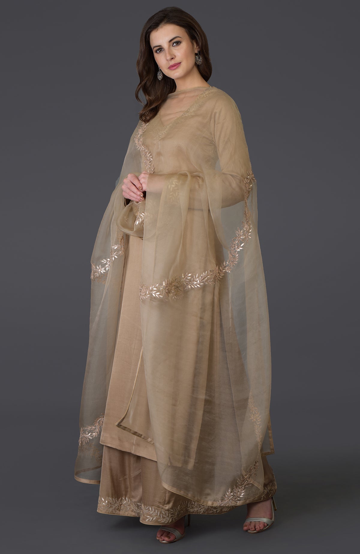 A woman models a beige Gota Patti work farshi palazzo suit with a sheer dupatta.