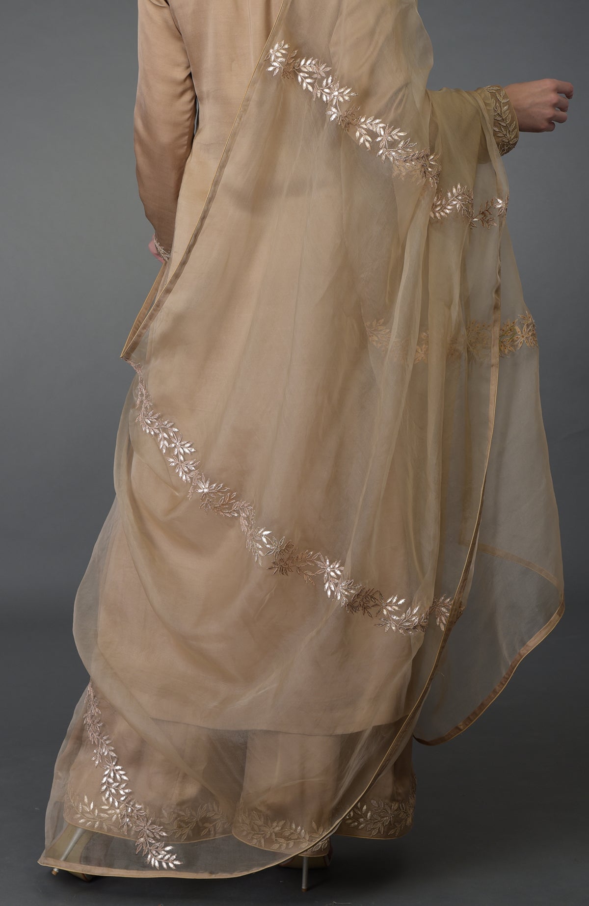 A woman models a beige Gota Patti work Farshi Palazzo Suit with a sheer dupatta.