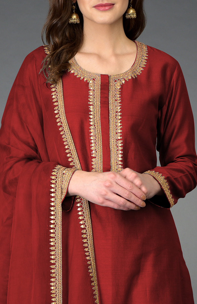 A woman models a red palazzo suit with gold marori and sequin embroidery.