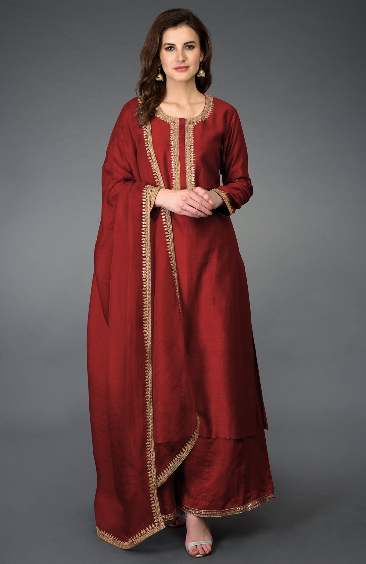 A woman models a red palazzo suit with gold embroidery and a matching dupatta.