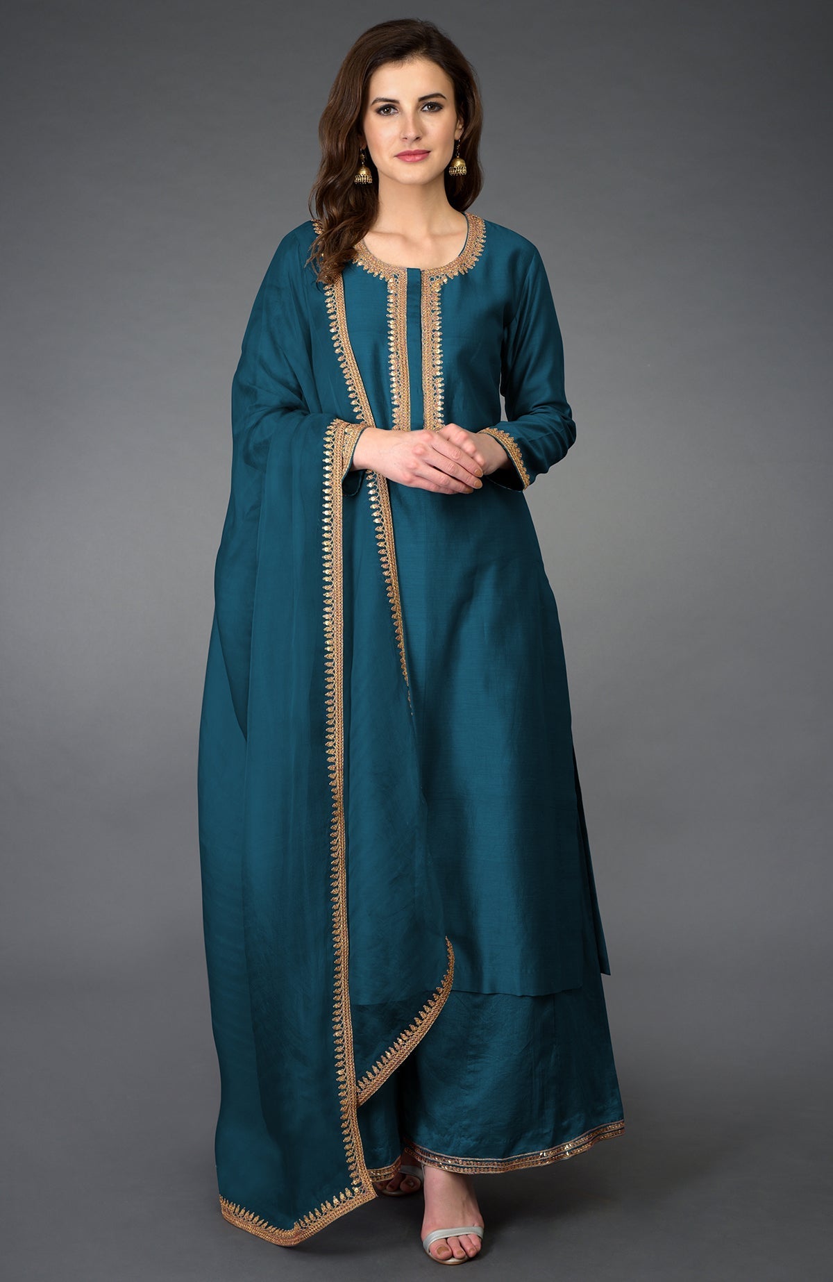 A woman models a teal palazzo suit with gold embroidery.