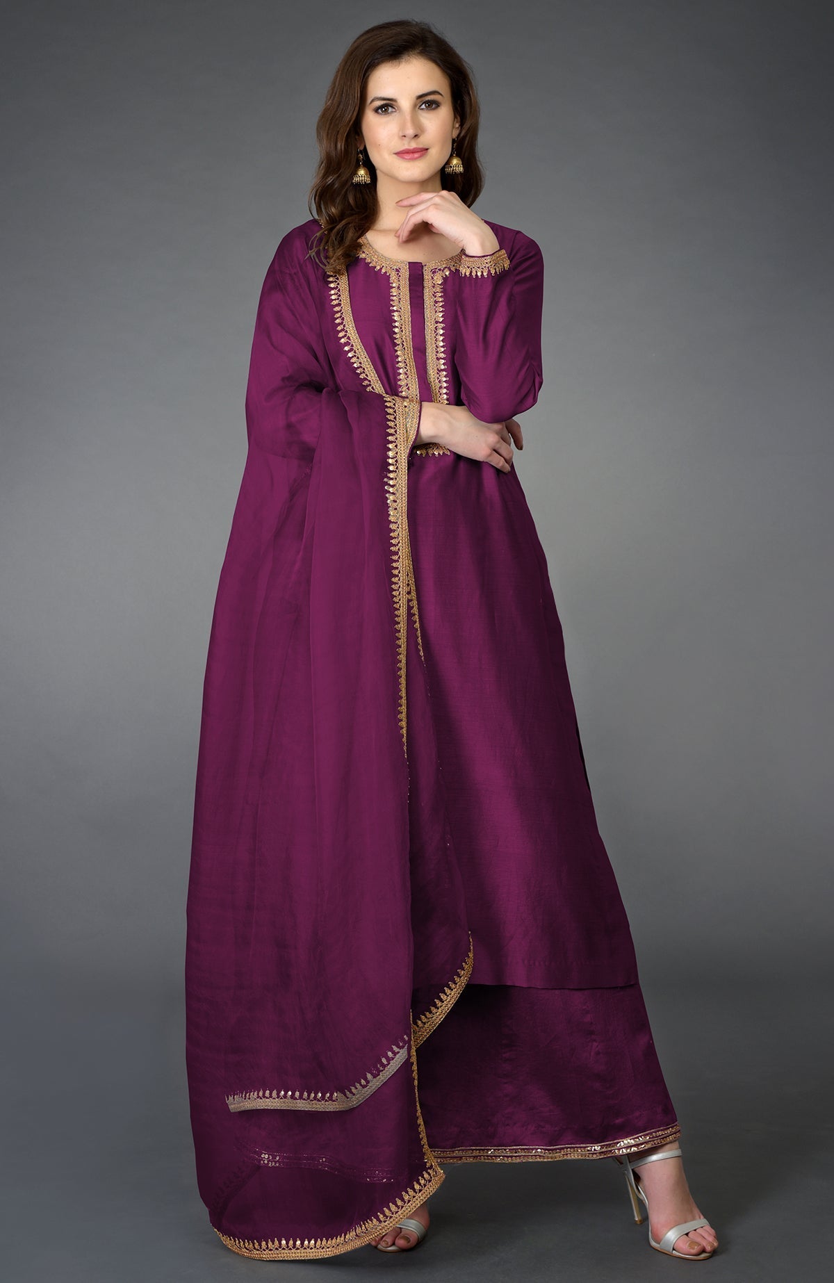 A woman models a purple palazzo suit with gold embroidery and a matching dupatta.