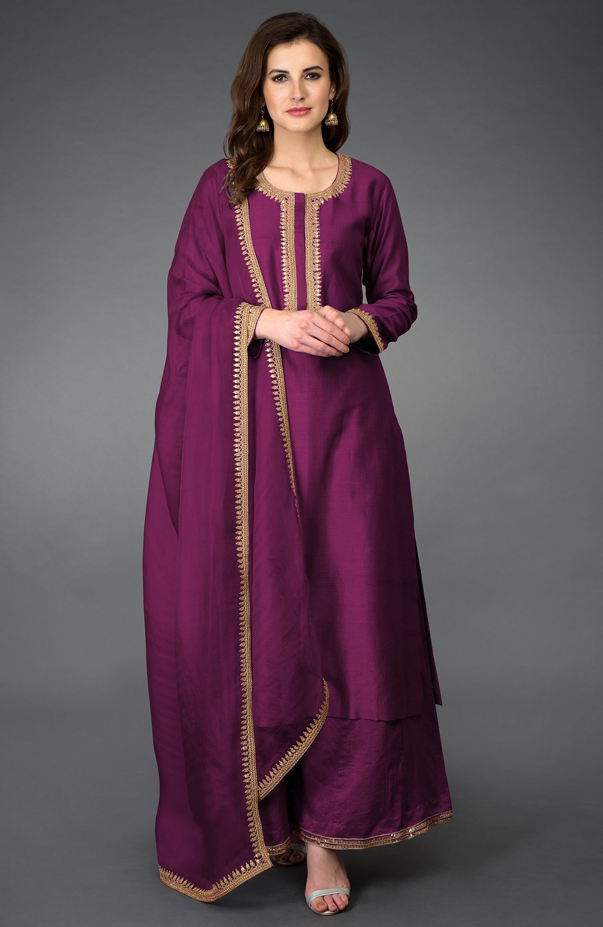 A woman models a purple palazzo suit with gold embroidery and a matching dupatta.