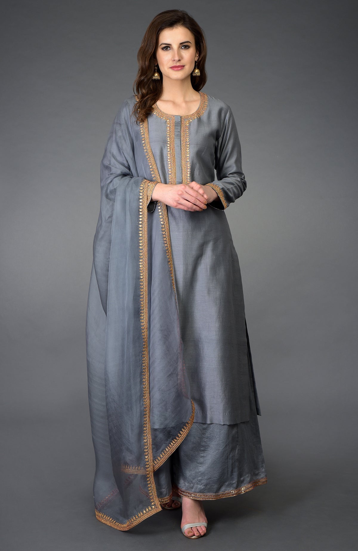 A woman models a grey palazzo suit with gold embroidery and a matching dupatta.