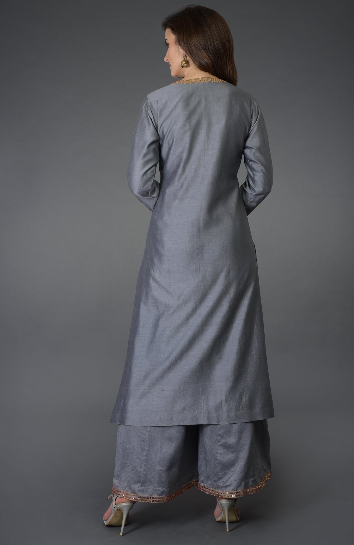 A woman models a grey marori and sequin work farshi palazzo suit from the back.