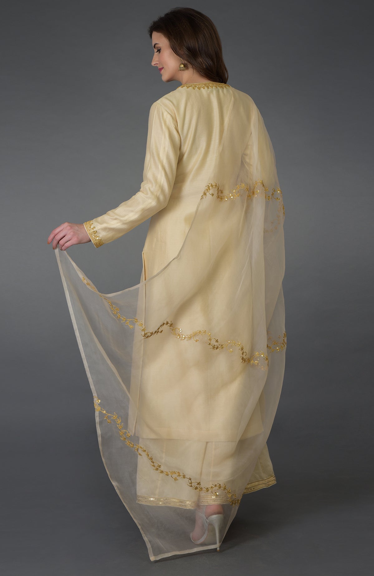 A woman models a cream marori and sequin work farshi palazzo suit with a sheer dupatta.