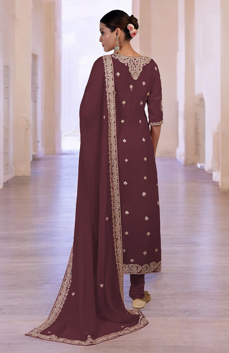A woman in a burgundy kurta set with gold embroidery stands facing away.