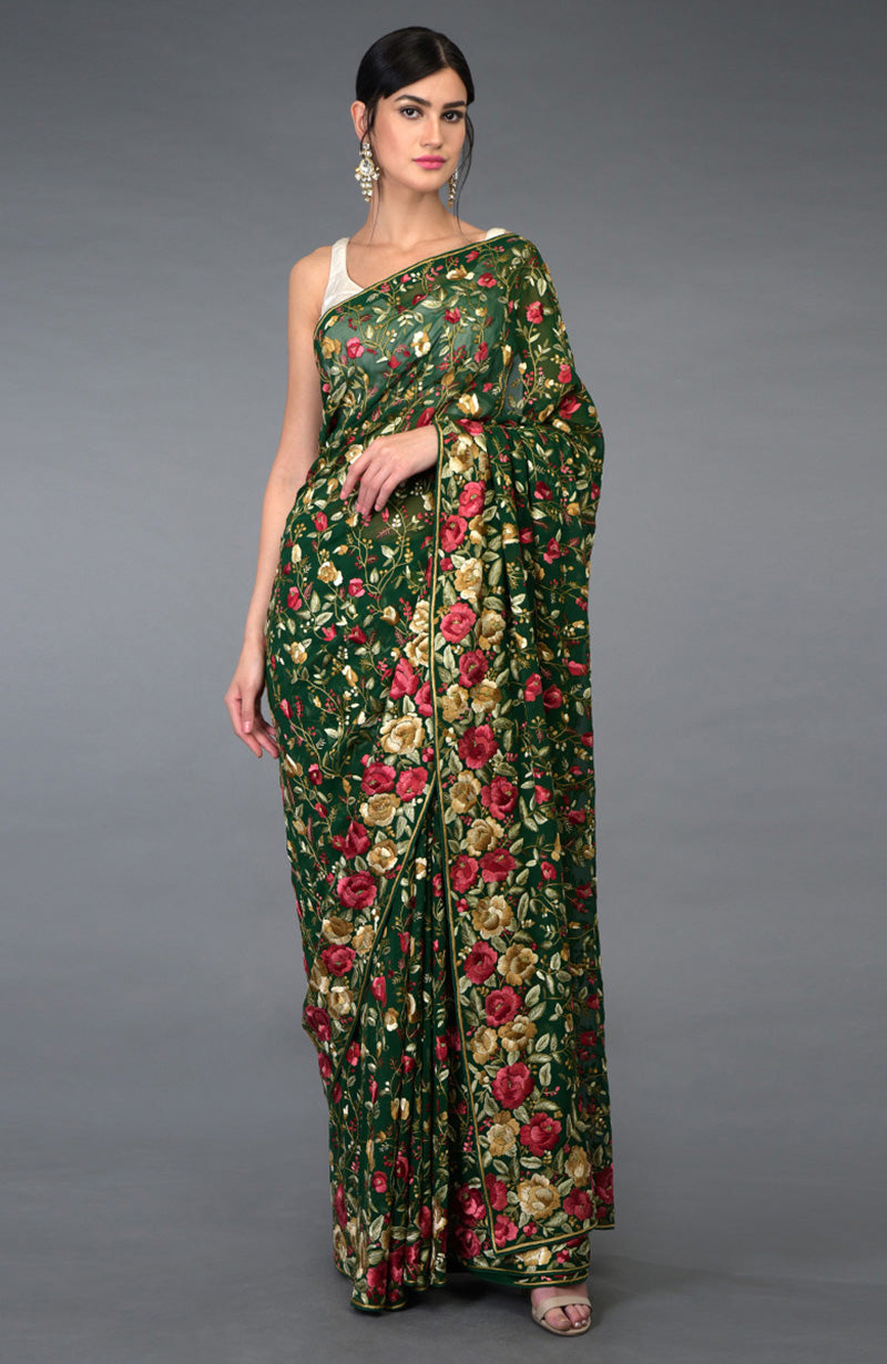 A woman models an emerald green Parsi Gara hand-embroidered saree with floral patterns.