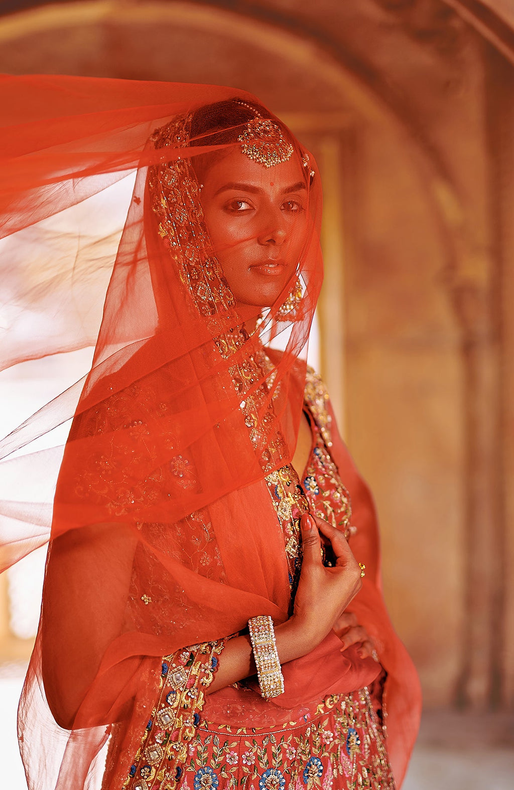 Red lehenga set with multicolour embroidery, gold detailing, peacock tassels, and sheer dupatta.