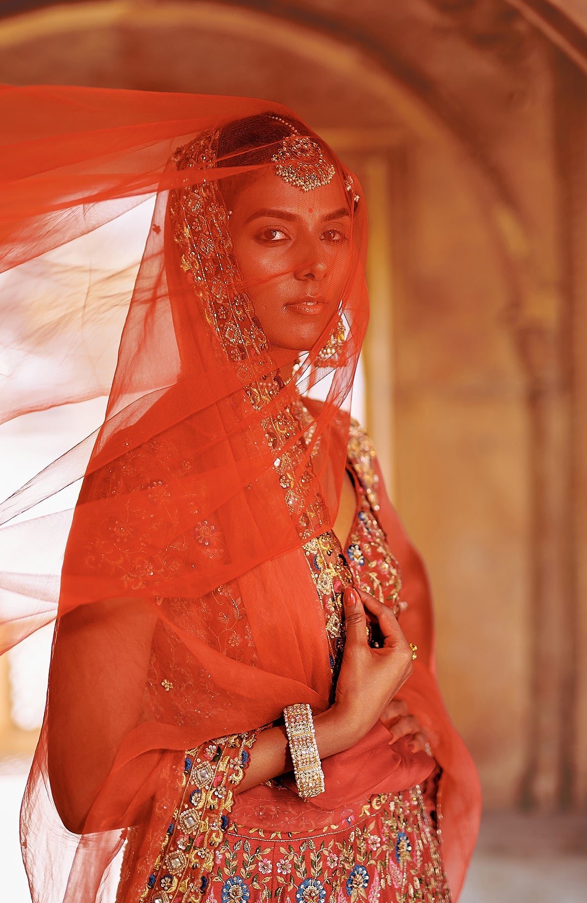 Red lehenga set with multicolour embroidery, gold detailing, peacock tassels, and sheer dupatta.
