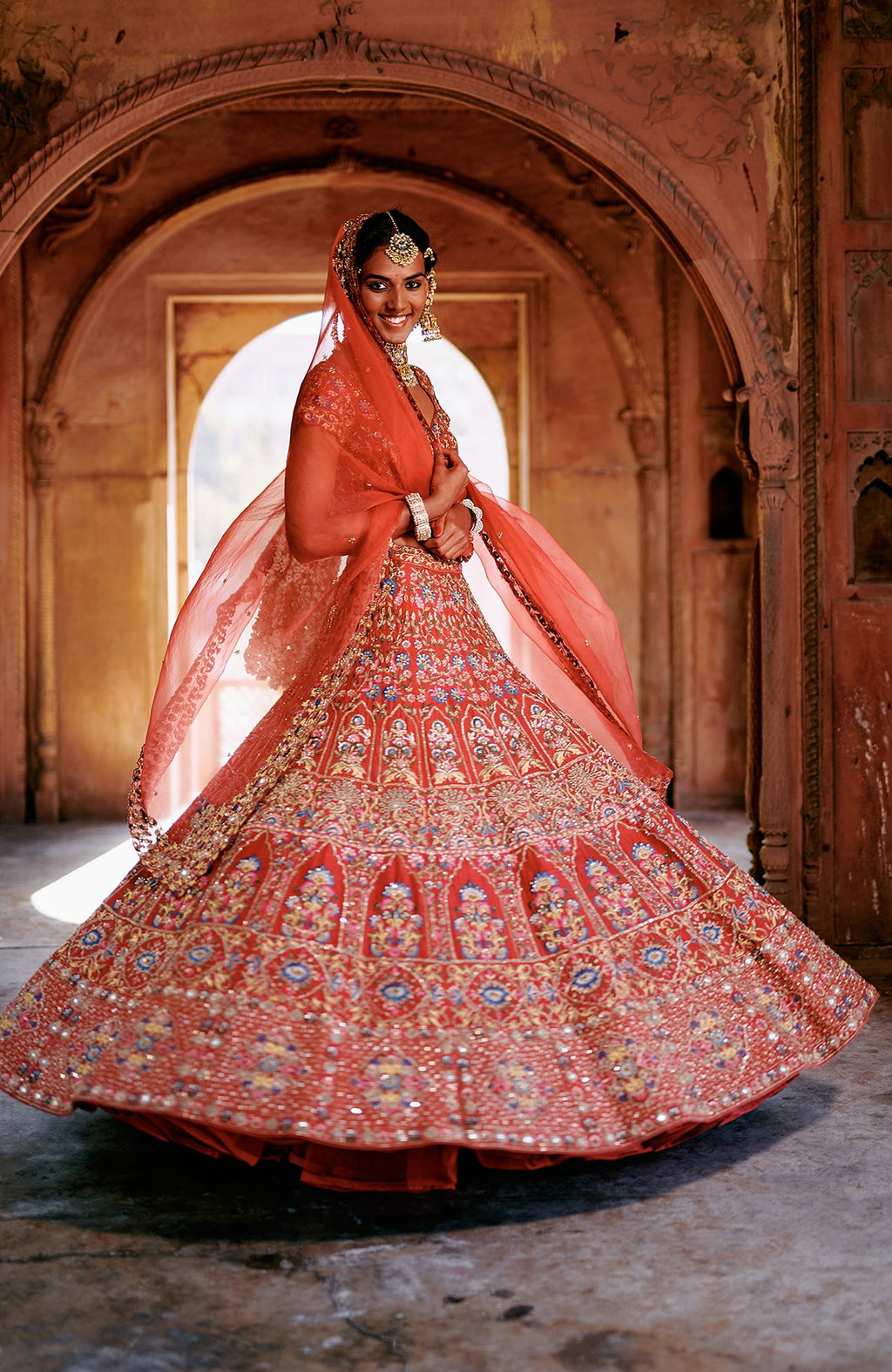 Red multicolour lehenga set with intricate embroidery, mirror work, and peacock feather tassels.