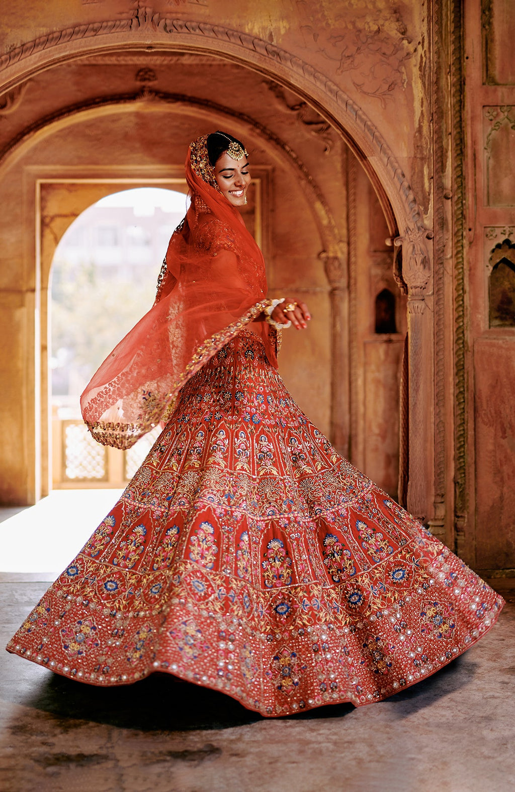 Red multicolour lehenga set with intricate embroidery, peacock tassels, and sheer dupatta.