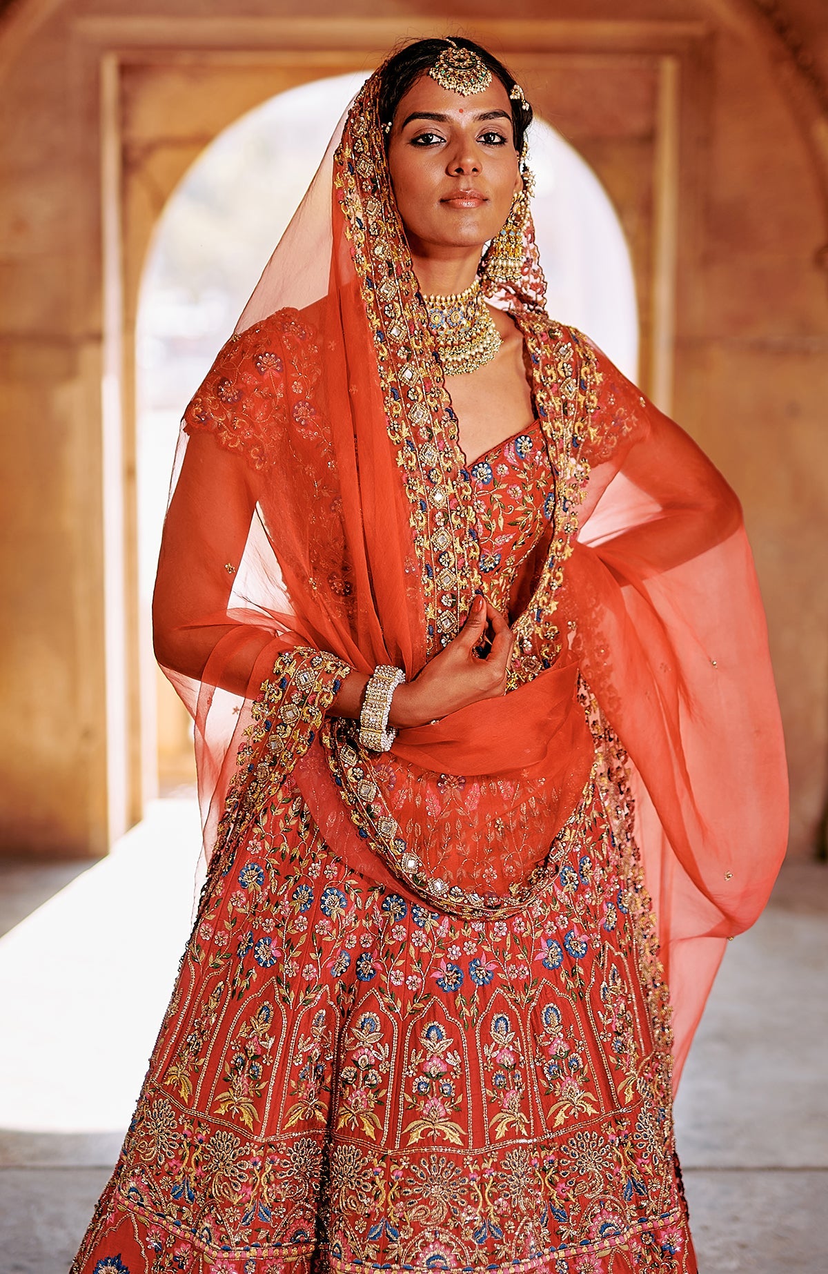Red multicolour lehenga set with intricate embroidery, peacock tassels, and sheer dupatta.