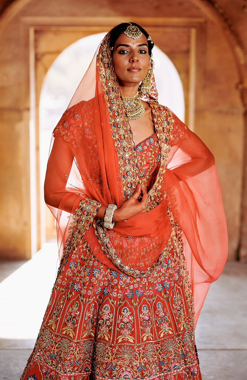 Red multicolour lehenga set with intricate embroidery, peacock tassels, and sheer dupatta.