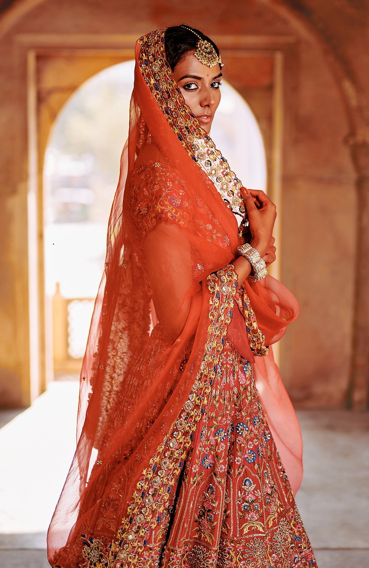 Red multicolour lehenga set with intricate embroidery, peacock tassels, and sheer dupatta.