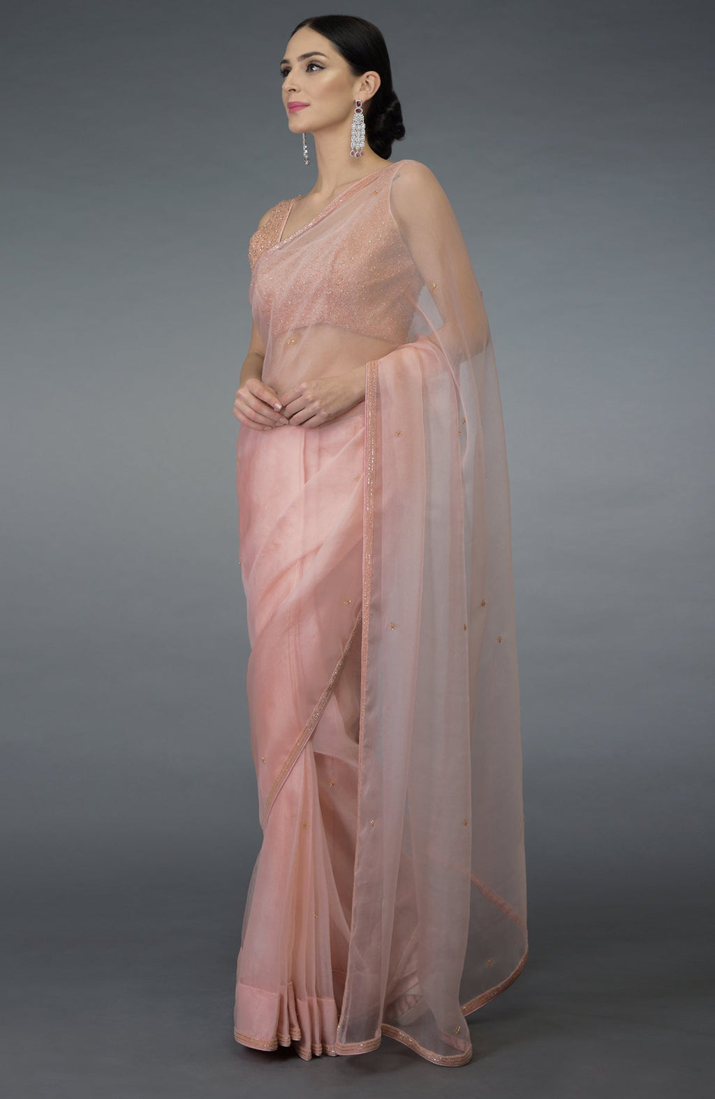 A woman models a pastel peach organza silk saree with a hand-embroidered blouse.