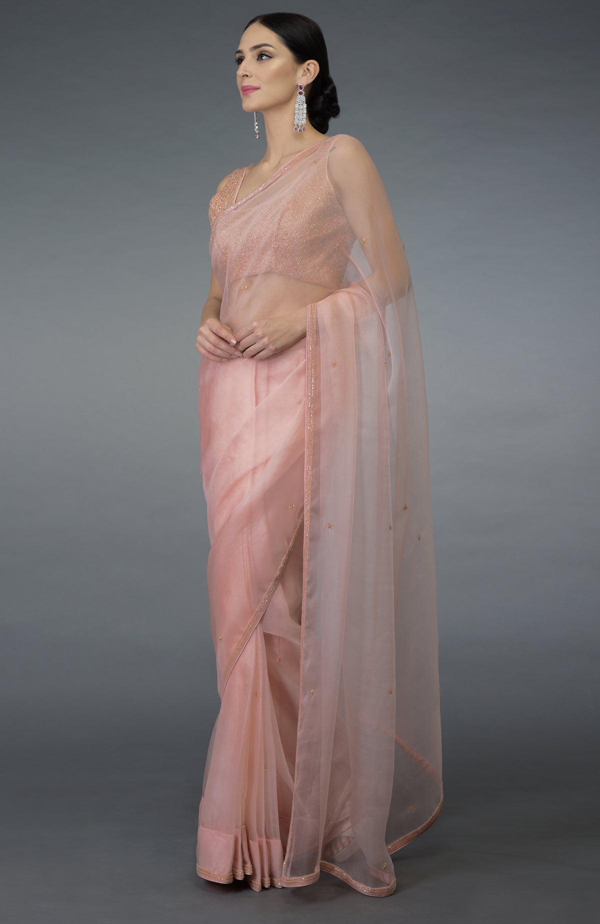A woman models a pastel peach organza silk saree with a hand-embroidered blouse.