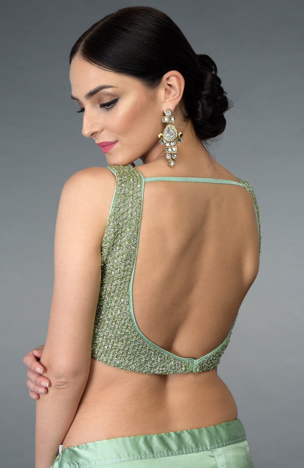 A woman models a mint green saree and a backless, beaded blouse.