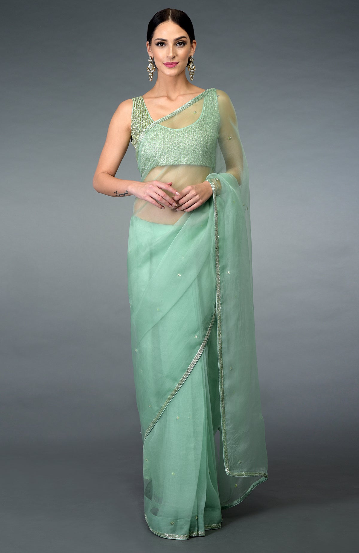 A woman models a mint green organza silk saree with a matching embroidered blouse.