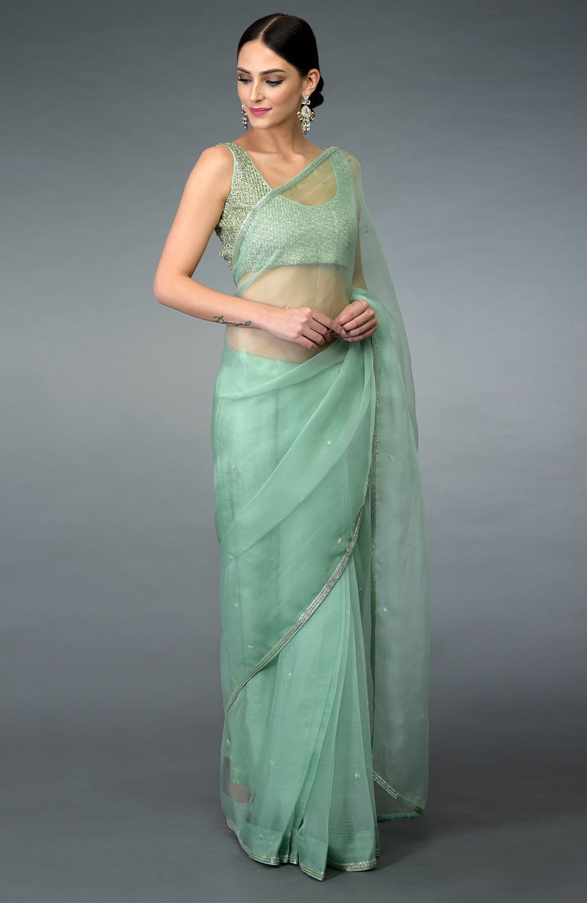 A woman models a mint green organza silk saree with a matching embroidered blouse.