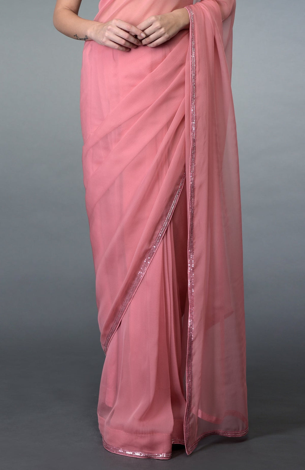 A woman models a pressed rose pure chiffon saree with sequin and bead borders.