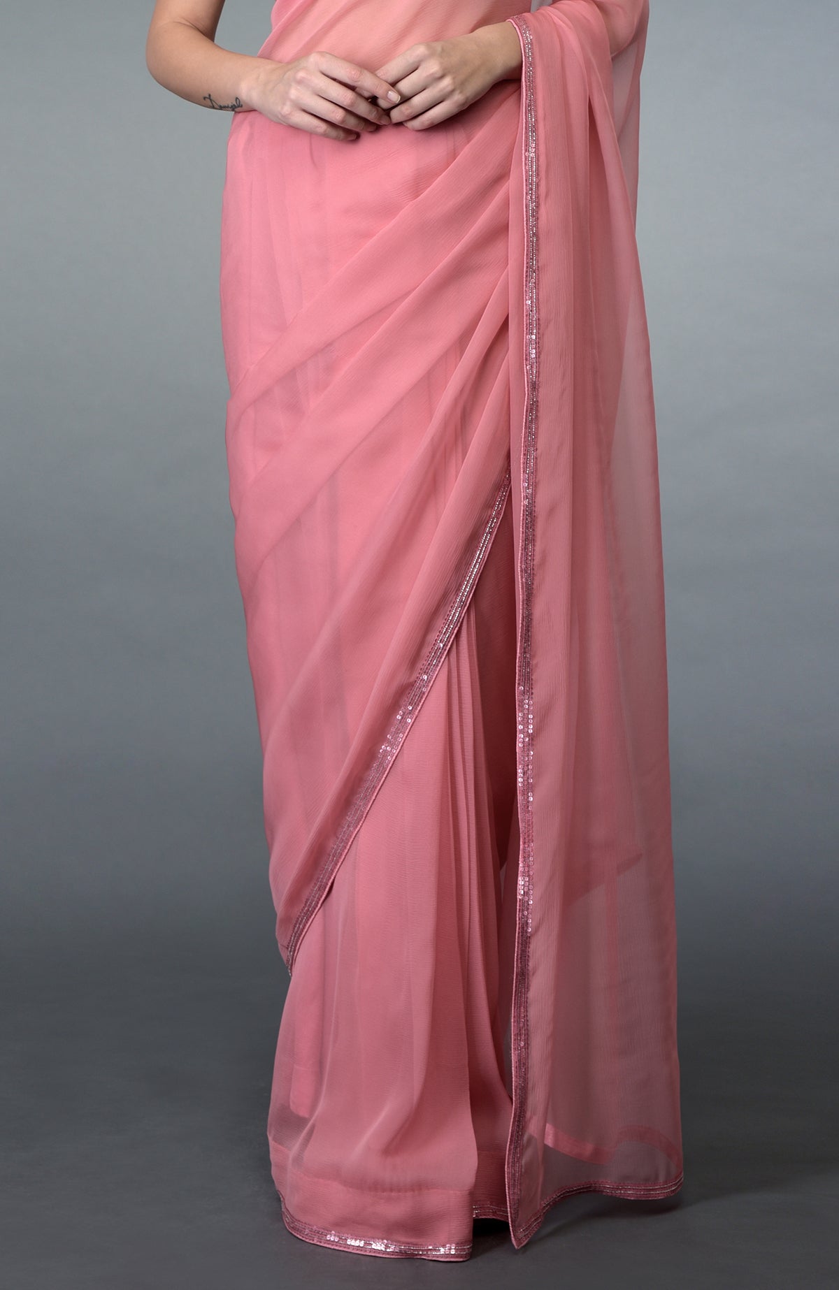 A woman models a pressed rose pure chiffon saree with sequin and bead borders.