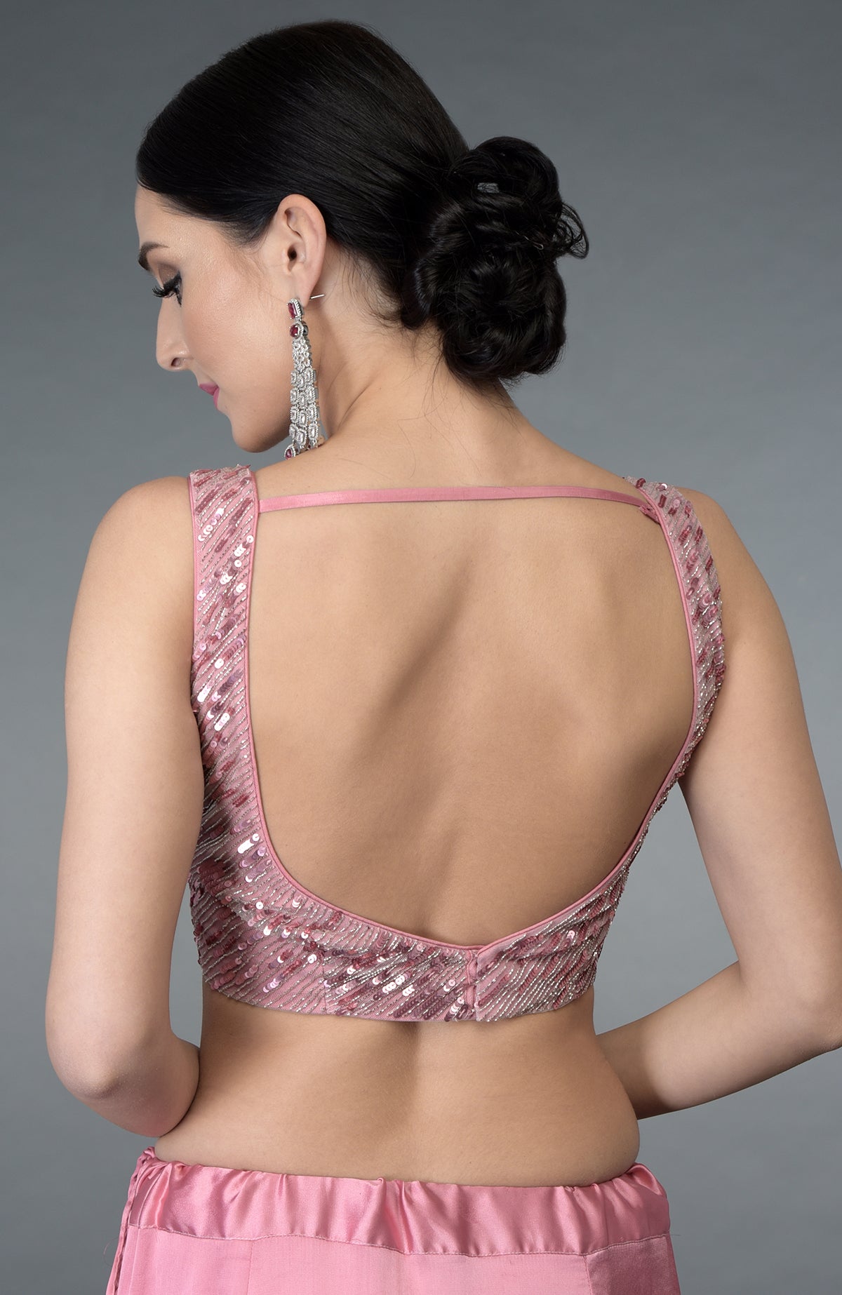 A woman models a pink sequin and bead embroidered blouse with an open back.