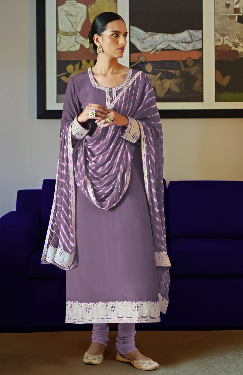 Woman in a purple kurta set with a leheriya dupatta and embroidered borders.