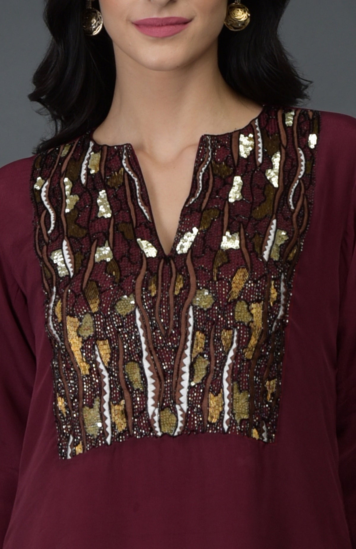 A woman models a burgundy tunic with intricate gold, brown, and white embroidery.