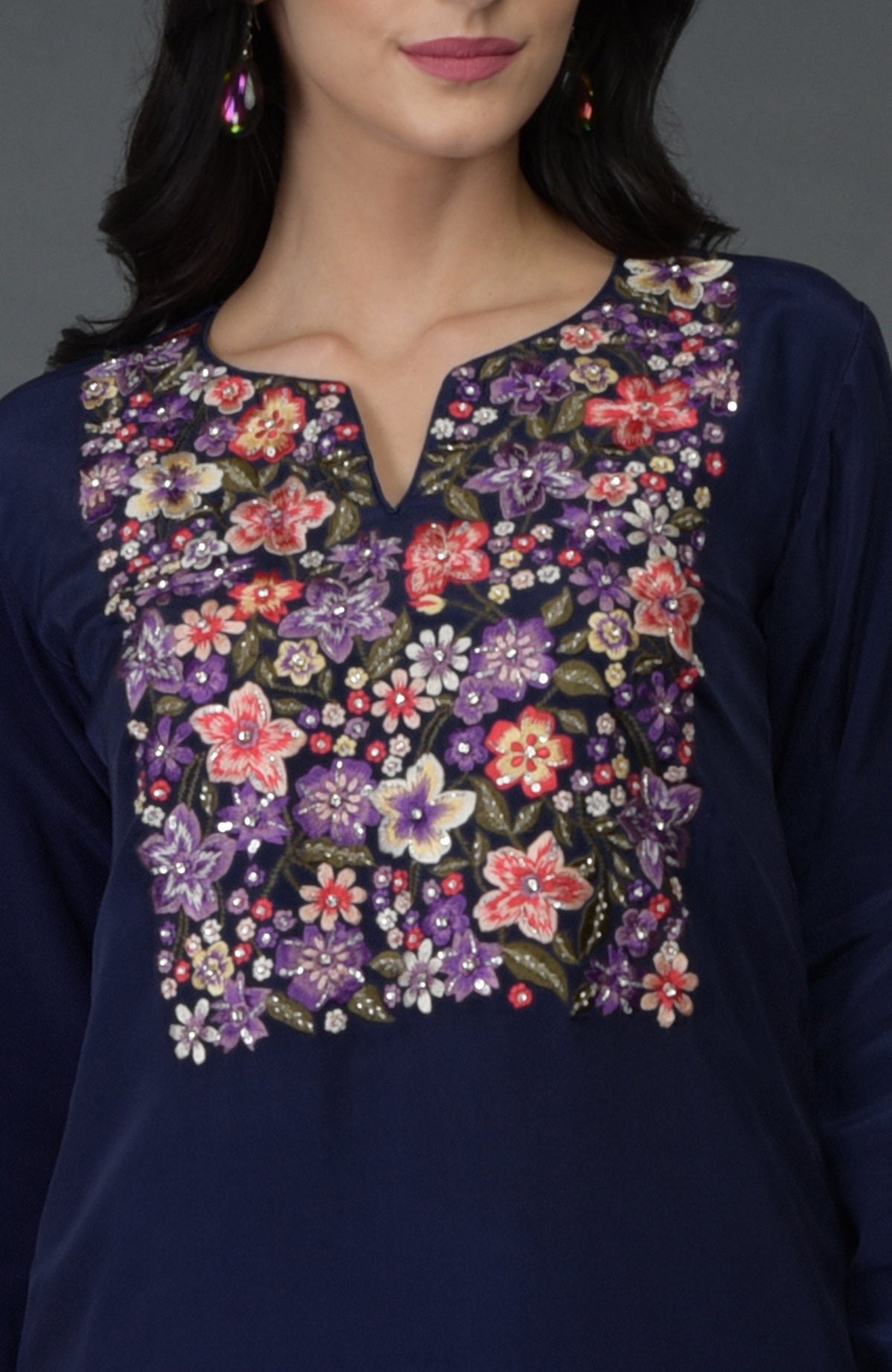 A woman models an eclipse blue top with colorful floral embroidery and sequins.