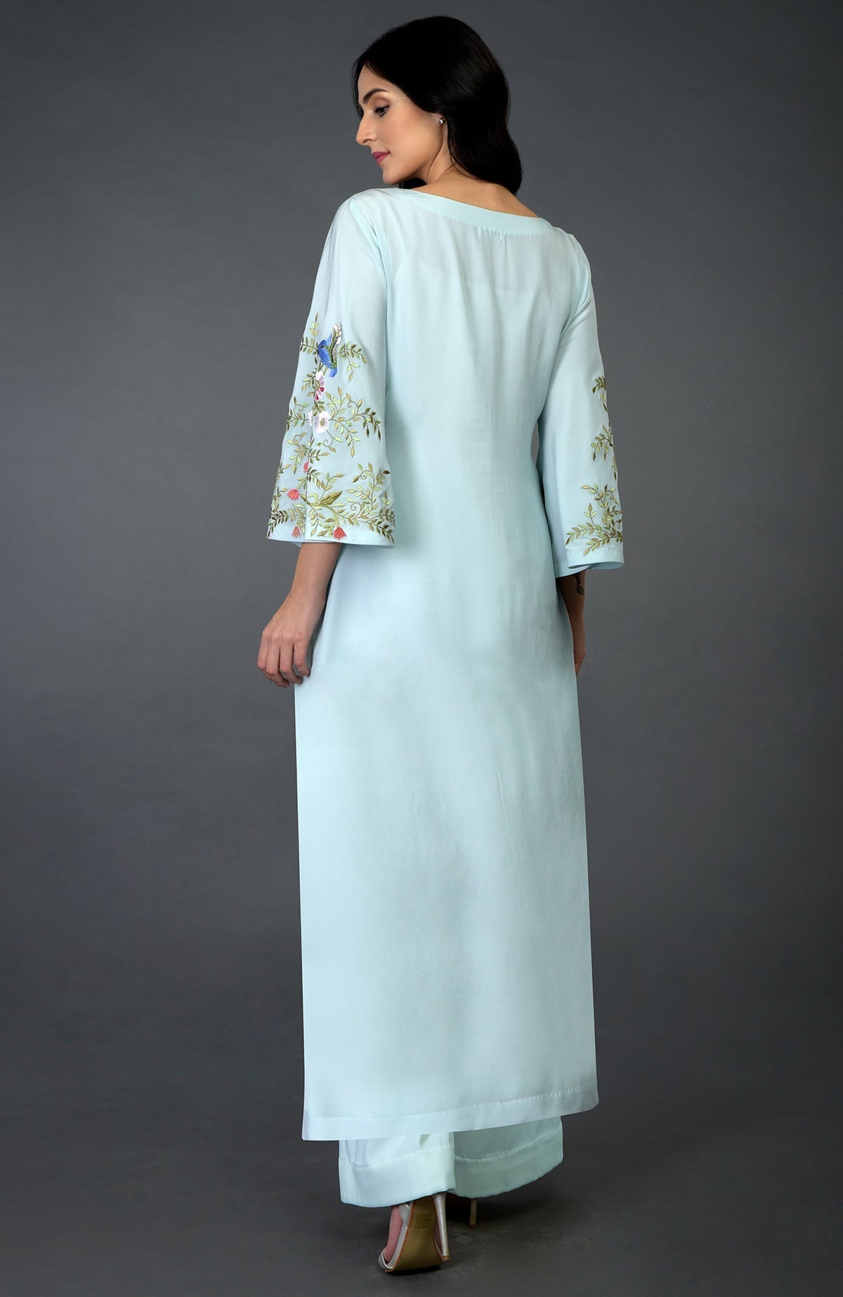 A woman models a serenity blue kurta set with bird and floral embroidery on the sleeves.