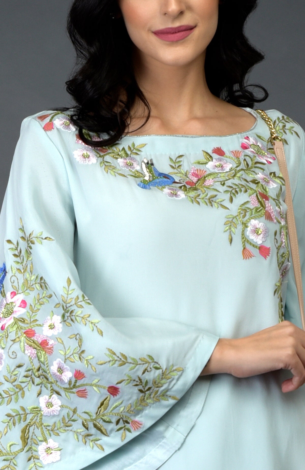A woman models a light blue kurta with colorful bird and floral embroidery.