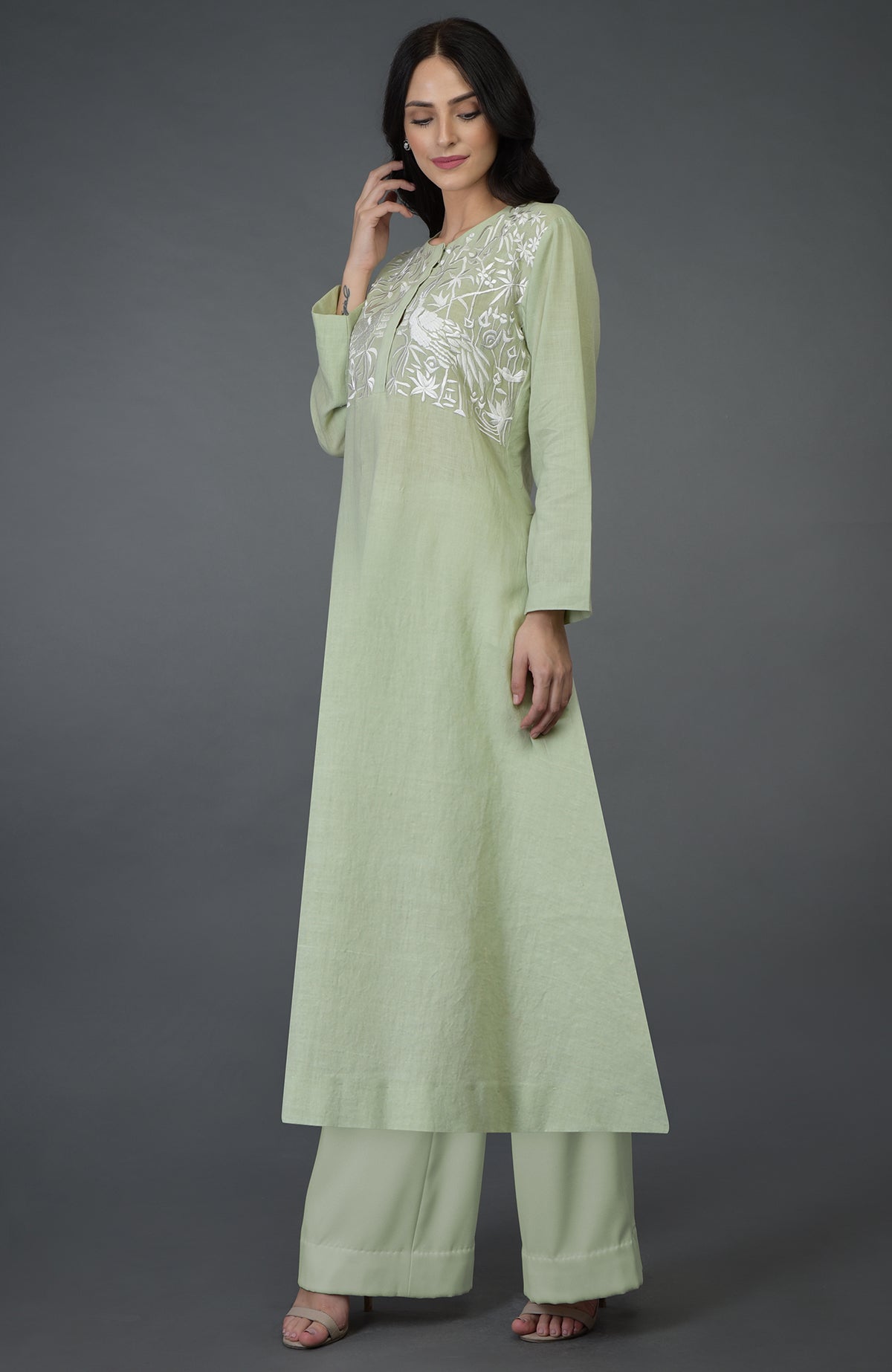 A woman models a pista green kurta set with white bird and floral embroidery.