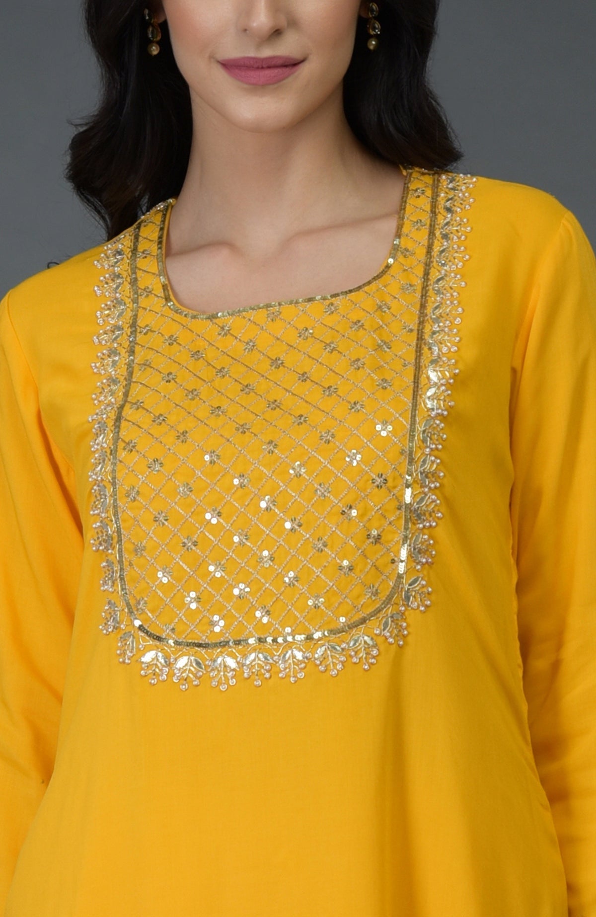 A woman models a sunglow yellow kurta with intricate gota, sequin, and pearl bead embroidery.