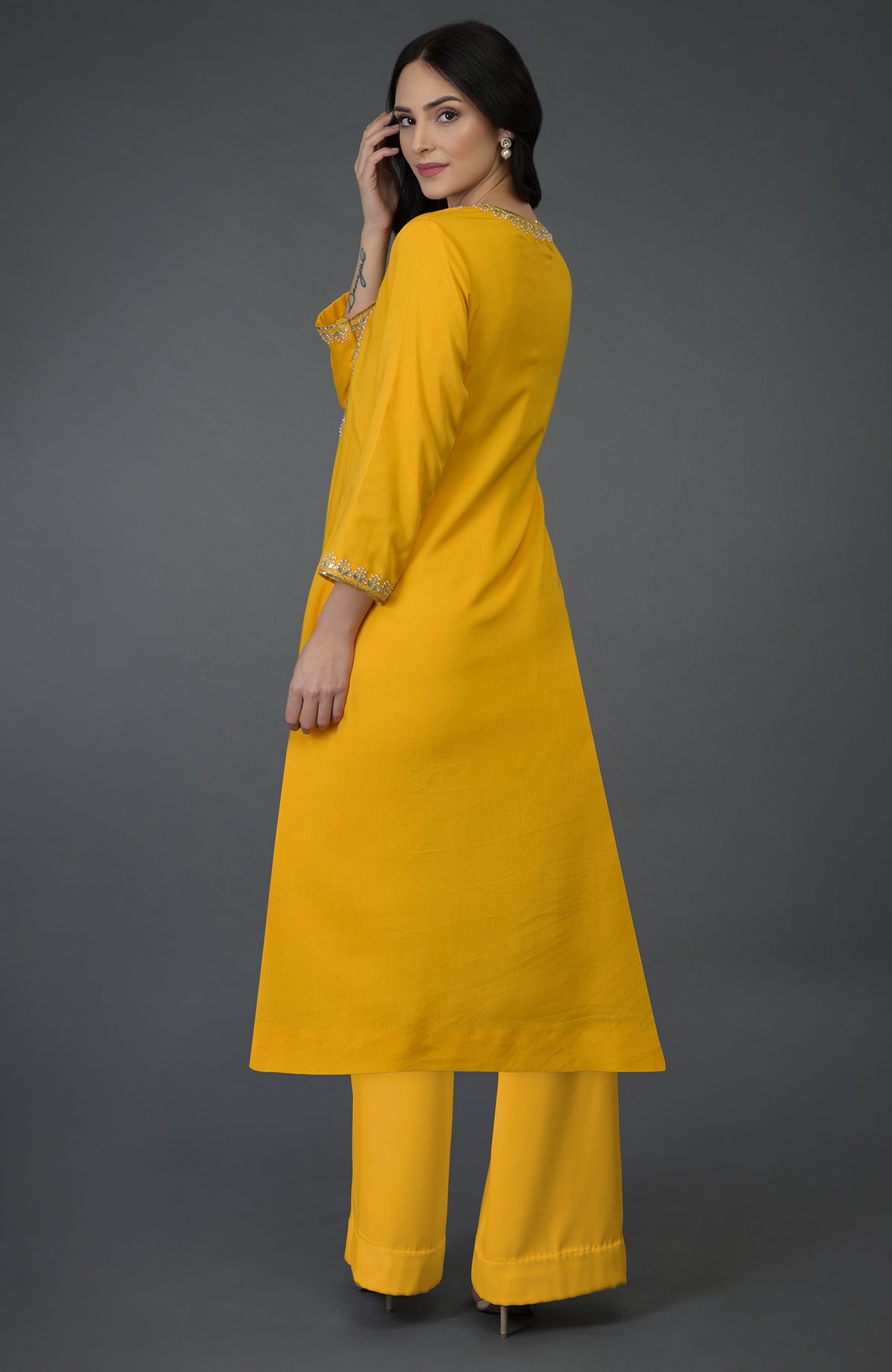 A woman models a sunglow yellow kurta set with gota, sequin, and pearl bead embroidery.