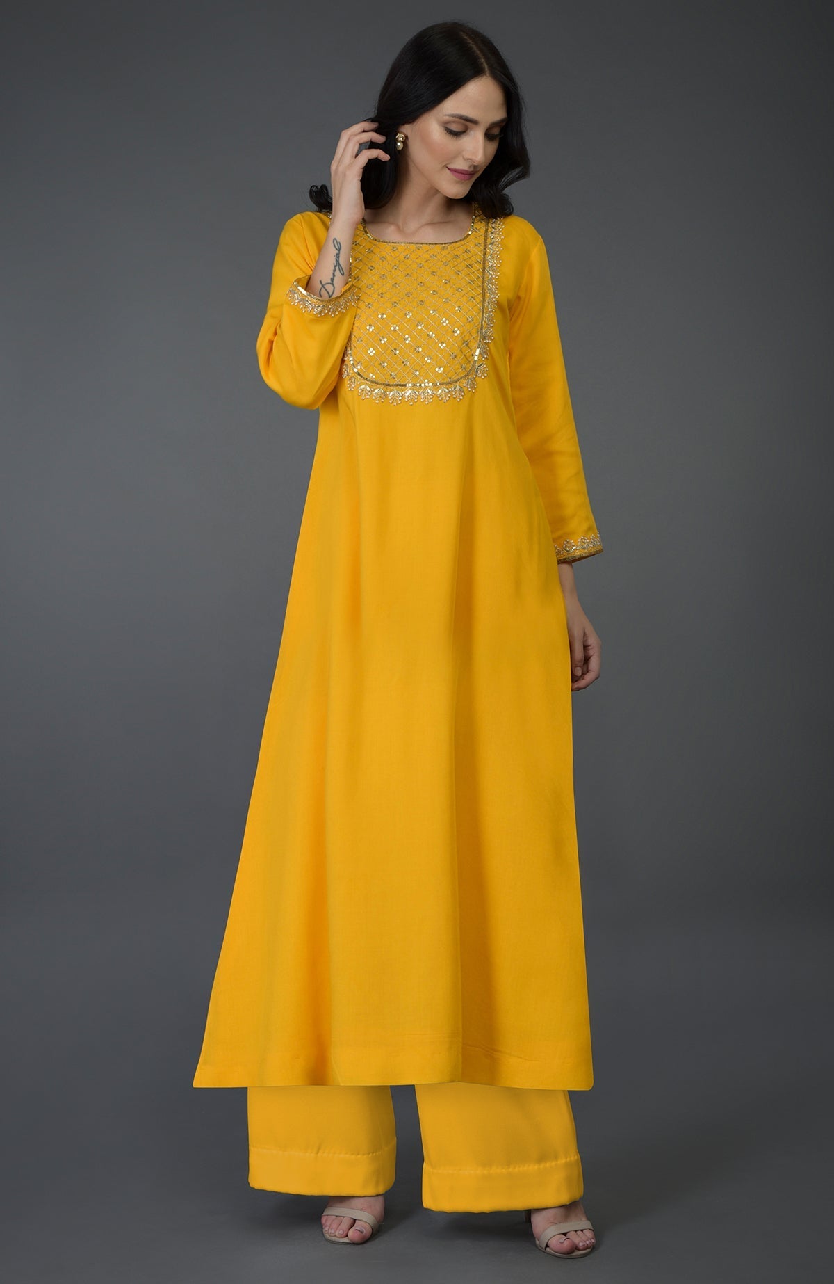 A woman models a sunglow yellow kurta set with gota sequin and pearl bead embroidery.