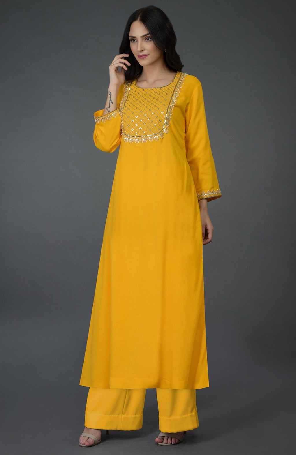 A woman models a sunglow yellow kurta set with gota, sequin, and pearl bead embroidery.