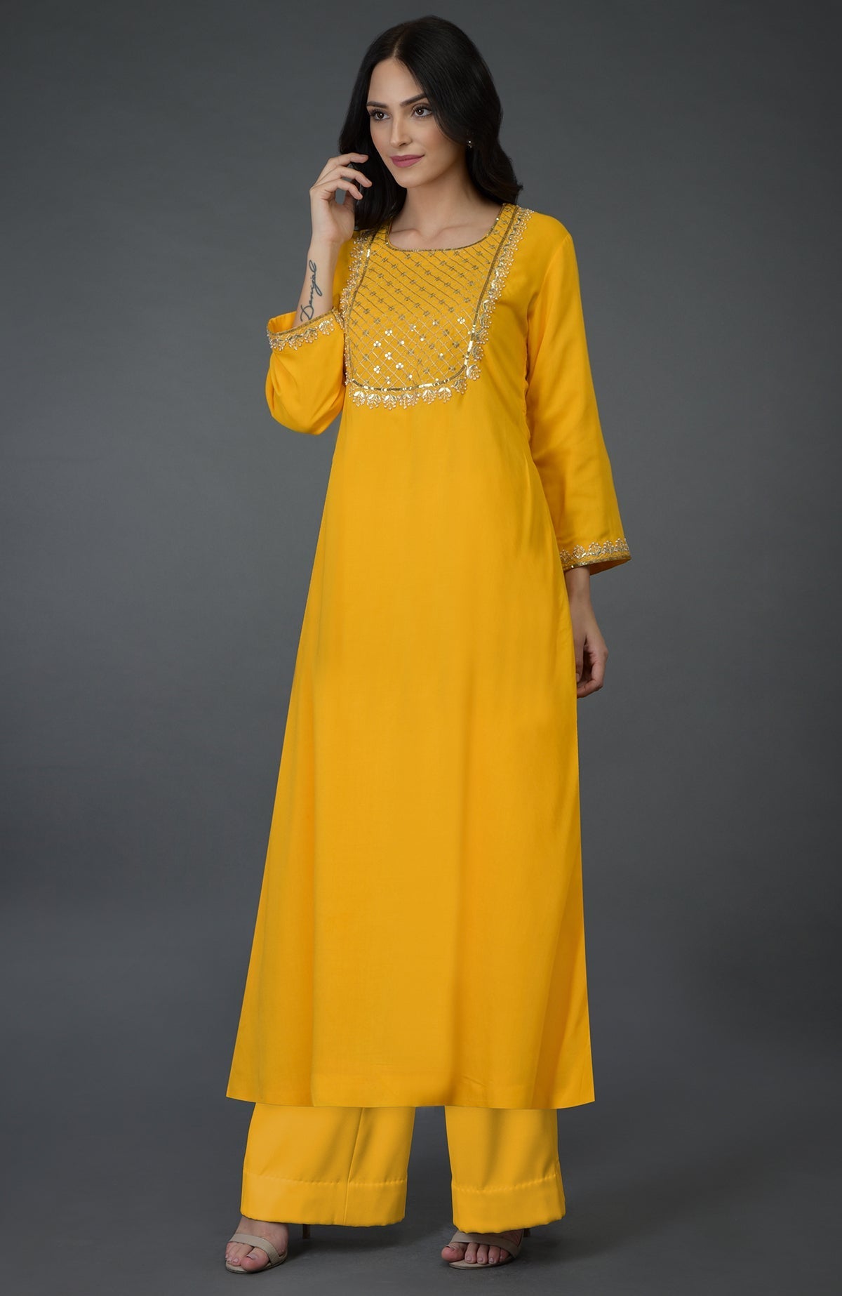 A woman models a sunglow yellow kurta set with gota, sequin, and pearl bead embroidery.